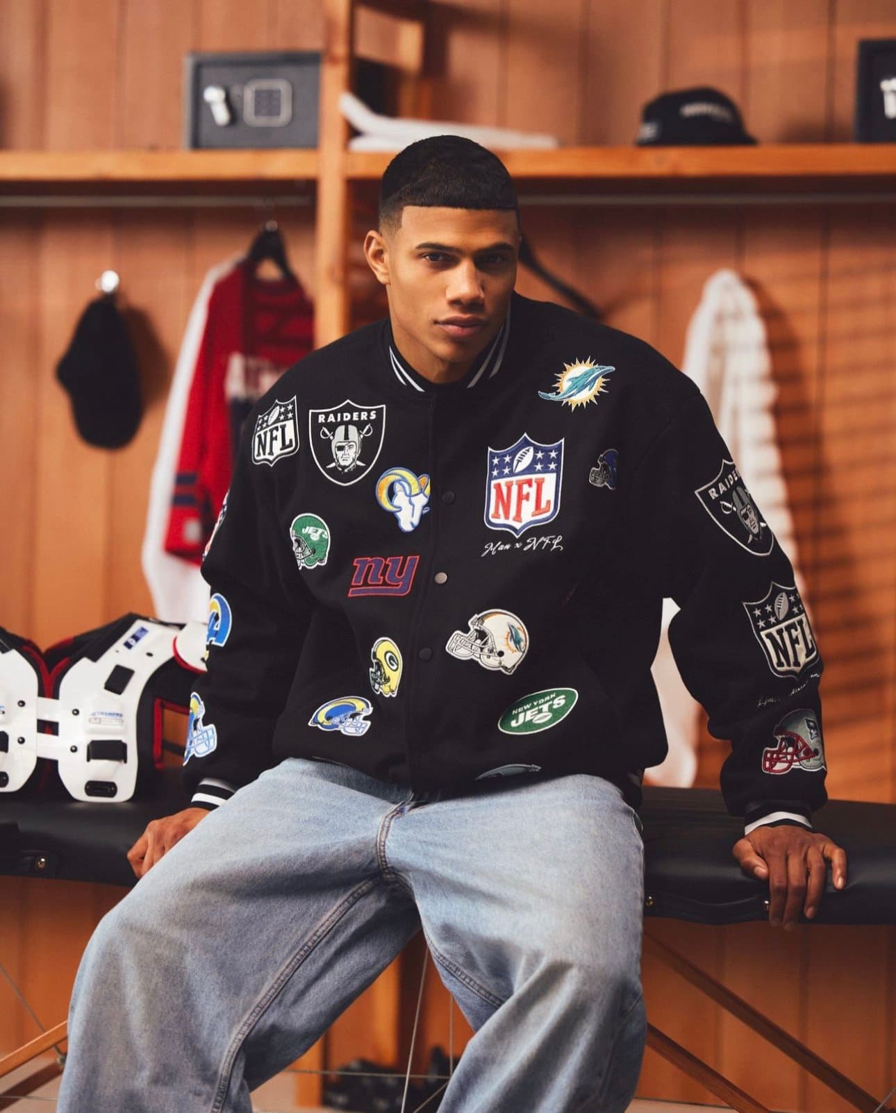 Model in an all-over NFL patch varsity jacket in a locker room